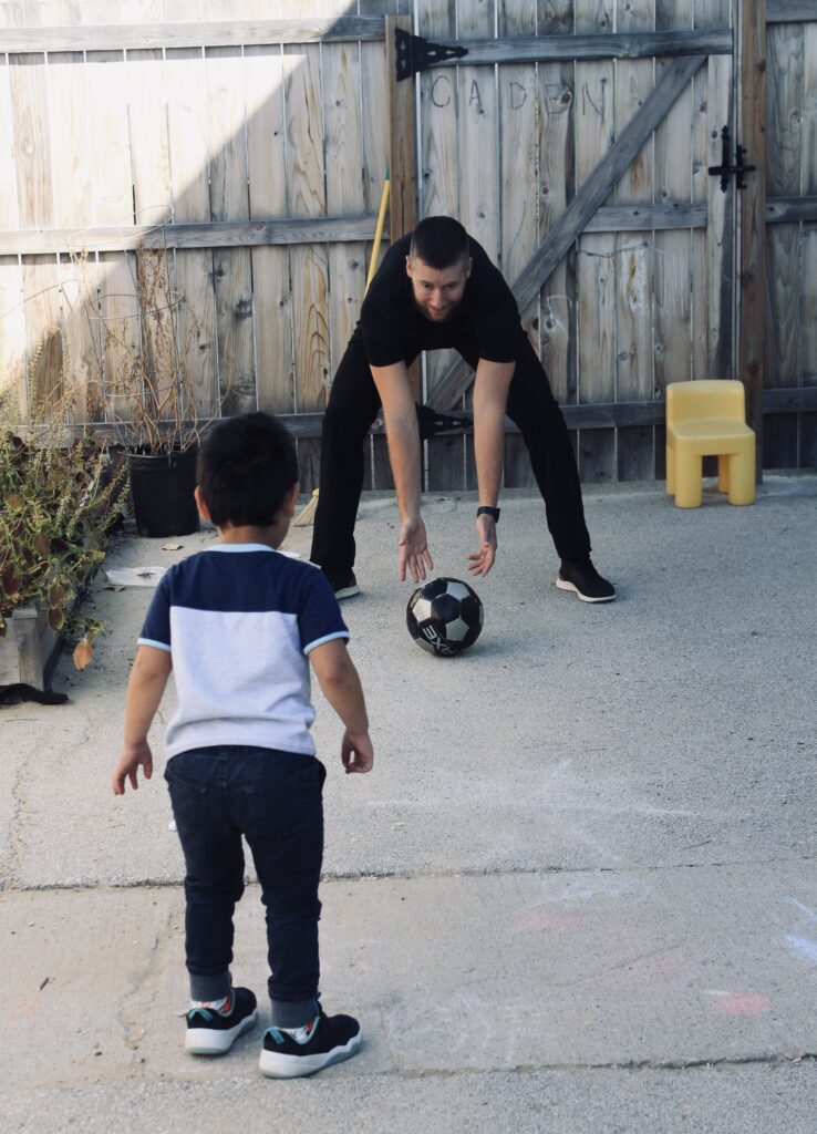 A boy and man playing with a soccer ball.