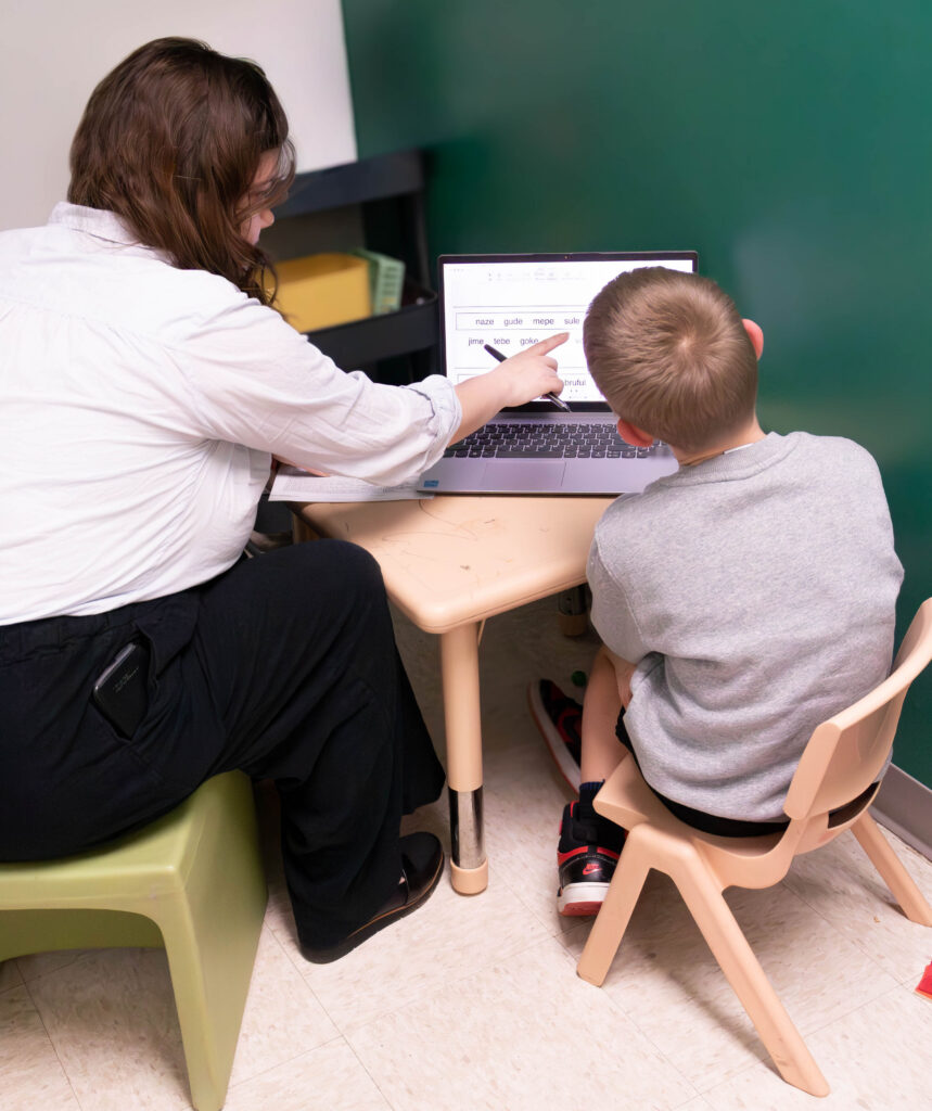 therapist sitting with boy and pointing to words on a computer 