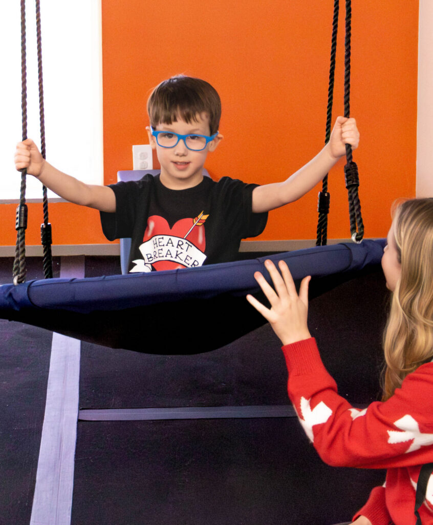 boy on a swing next to a woman kneeling on the ground with her hand on the swing