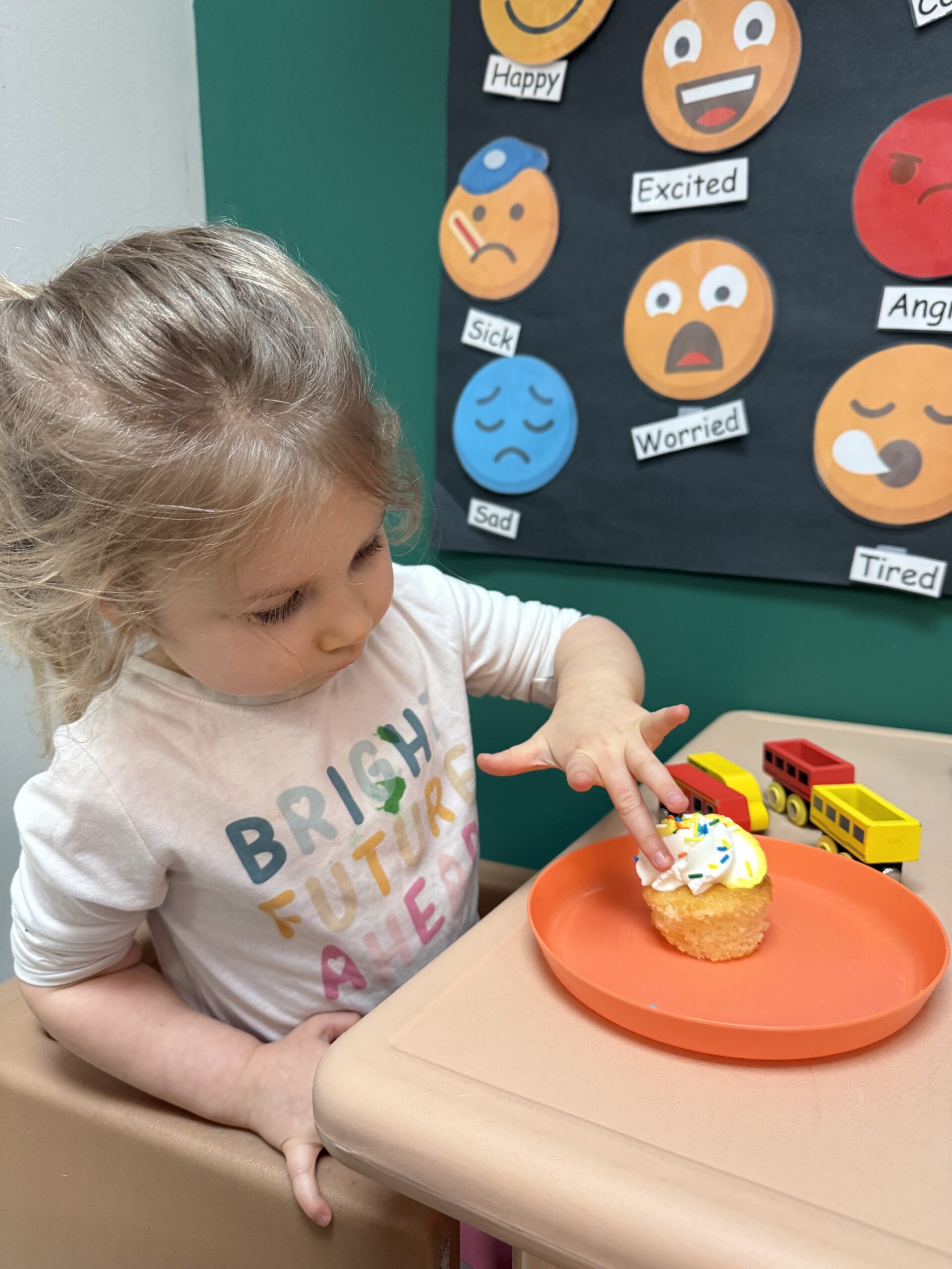 girl eating cupcake next to a "How are you feeling today" emotions wall
