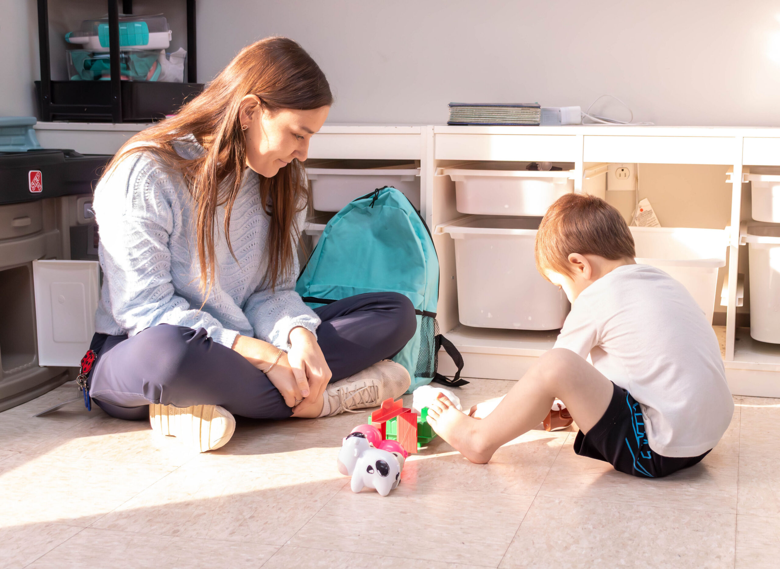 Woman and boy sitting on the floor with toys and a backpack