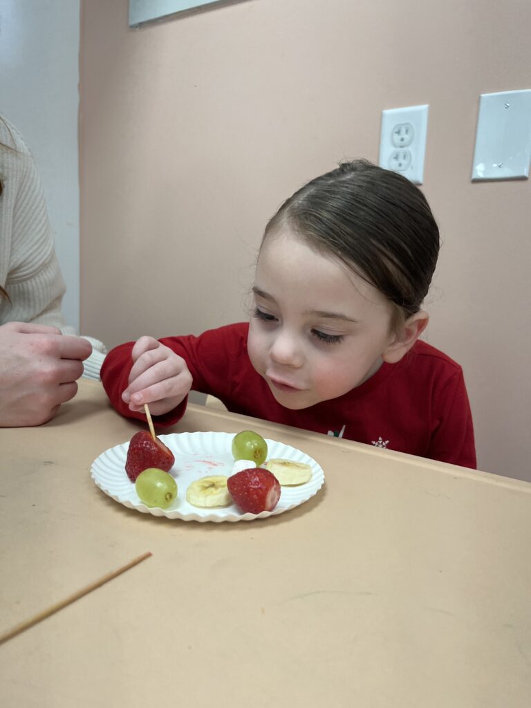 girl using toothpick to eat sliced fruit